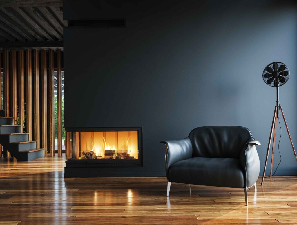 A black chair on a hardwood floor with a modern corner fireplace behind it on a black wall.