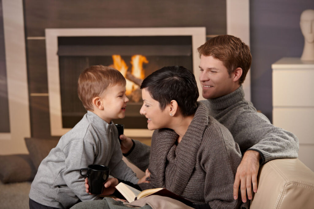 A mother, father, and son sitting together in front of a fireplace